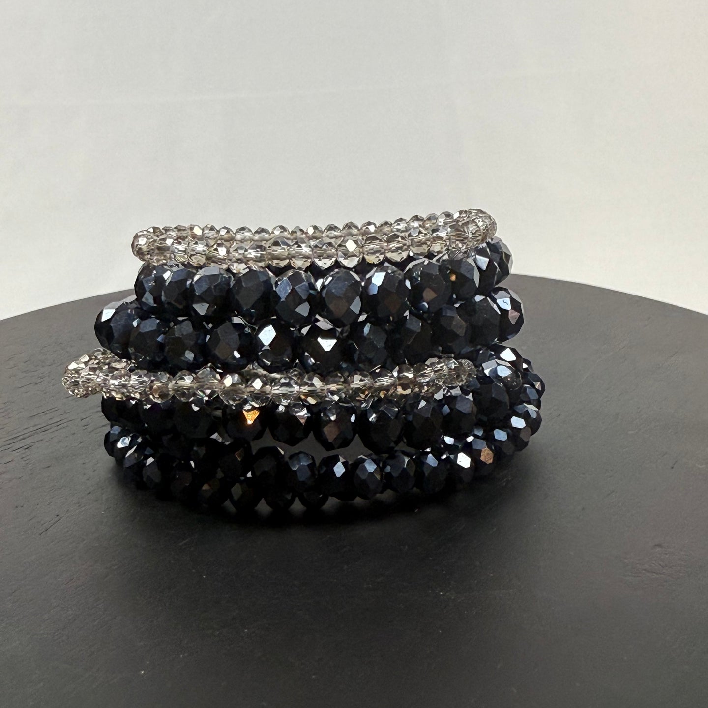 /Navy/ A stack of beaded bracelets with dark blue and clear faceted beads, displayed on a round black surface against a plain light gray background.