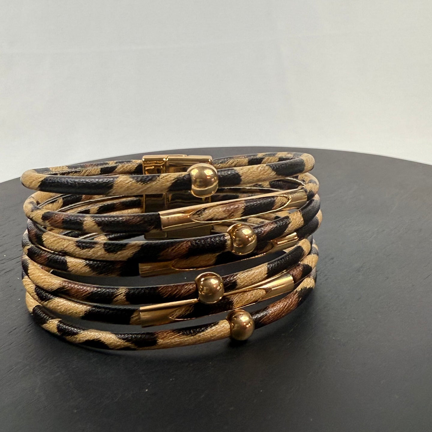 A stack of six animal print bracelets with gold magnetic clasps and gold bead accents, displayed on a dark round surface against a plain light background.