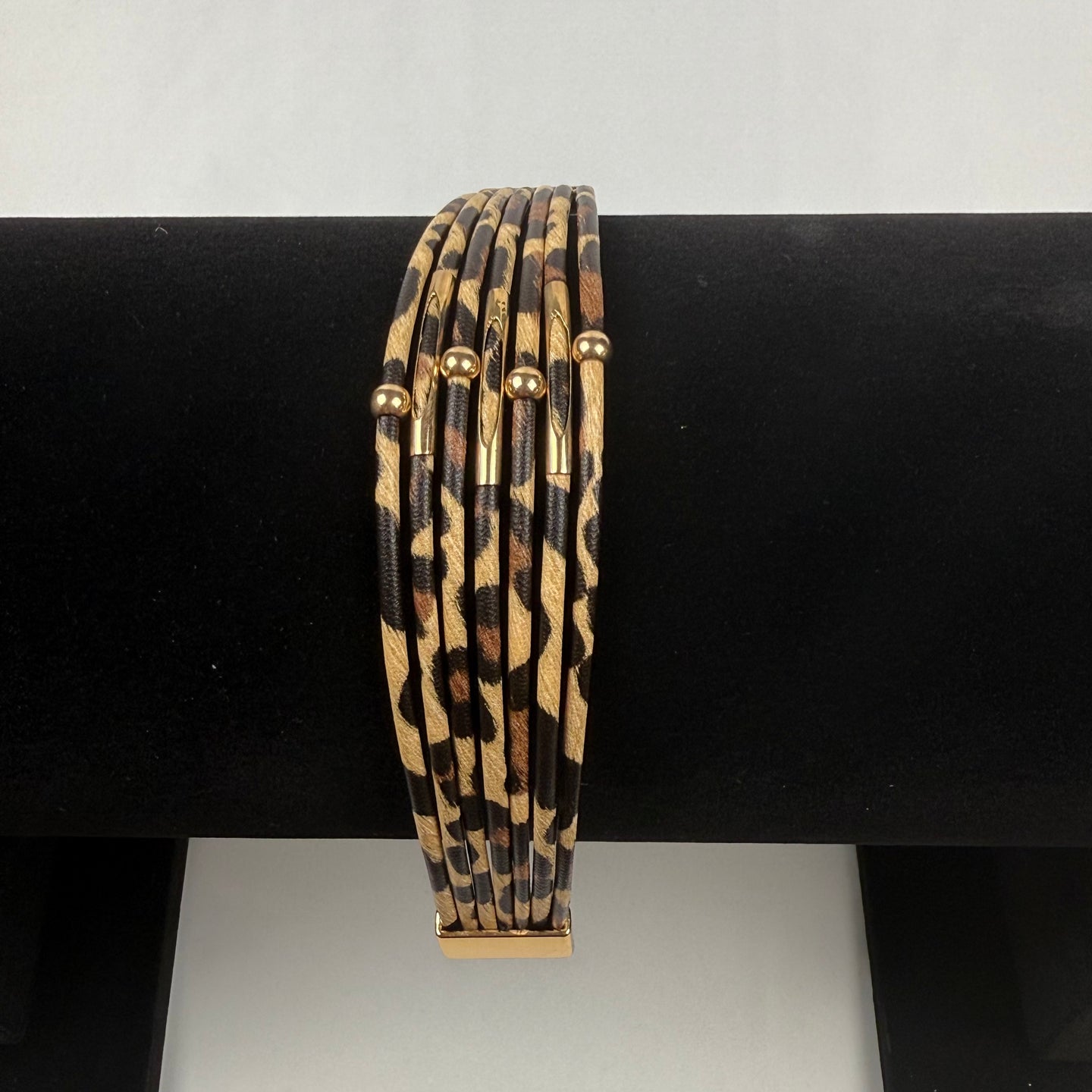 A set of six thin bangle bracelets with a leopard print pattern and small gold accents, displayed on a black bracelet stand.