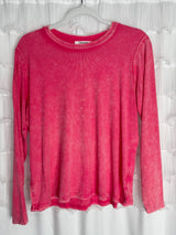 /Fuschia/ A long-sleeve, faded pink shirt hangs on a clear plastic hanger in front of a white textured curtain. The shirt has a ribbed neckline and visible stitching along the hems.