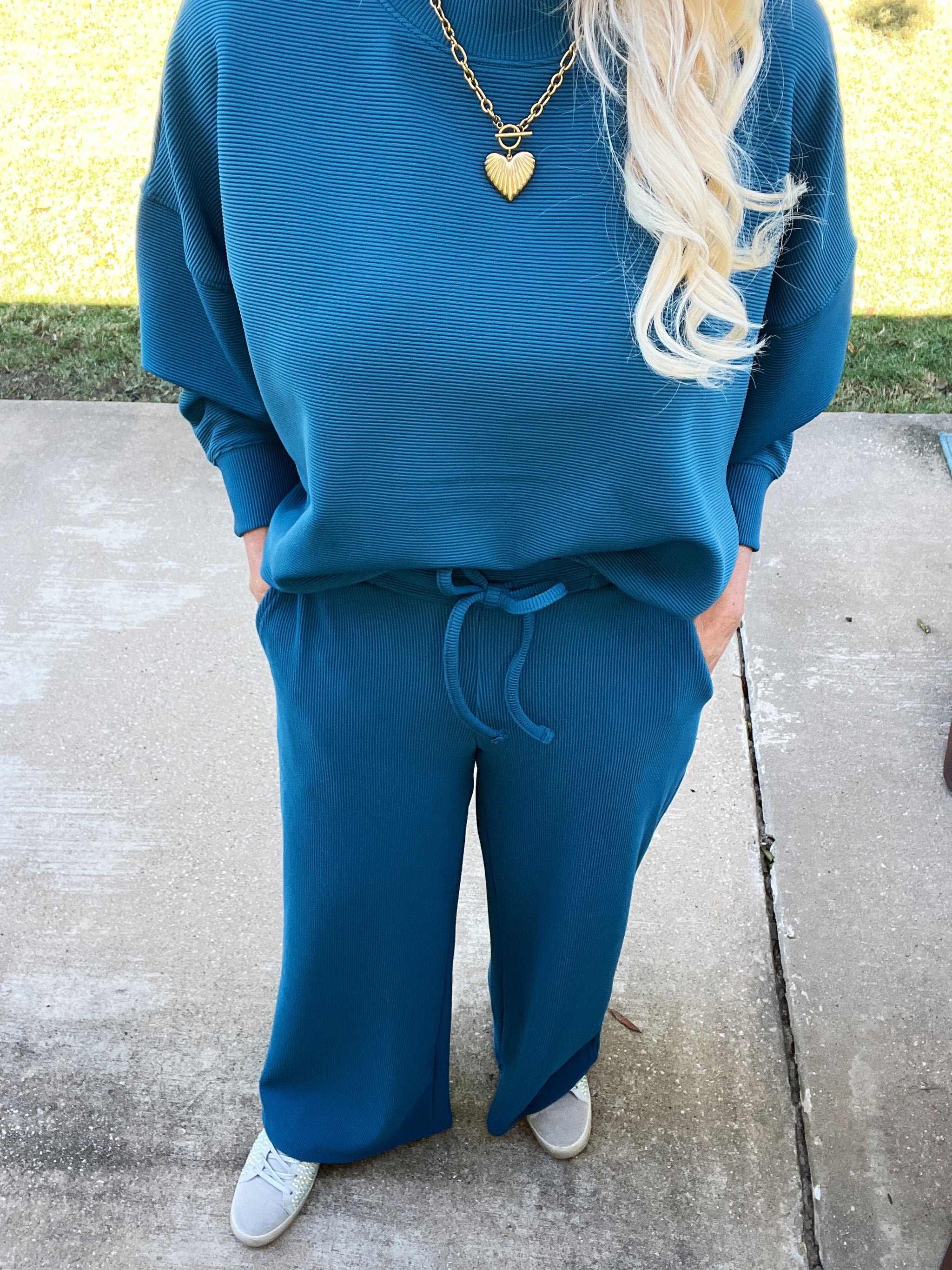 Person wearing a blue outfit with a heart-shaped necklace on a sidewalk.