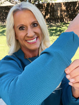 Woman wearing a blue sweater outdoors with a wooden fence in the background