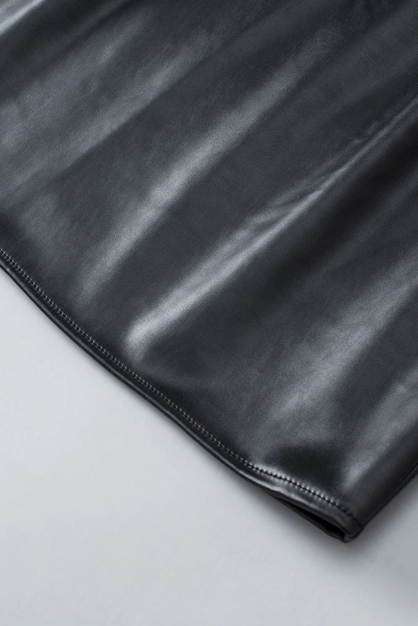 Close-up of the Kara Top by Lovesoft in shiny black faux leather, fully lined for comfort. The smooth texture, subtle reflections, and neat edge stitching are shown as it lies on a light gray surface.