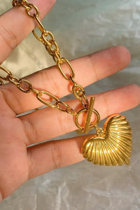 Gold chain bracelet with a shell charm held by a hand against a neutral background
