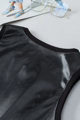 Close-up of the Kara Top by Lovesoft—a shiny black, sleeveless, fully lined top—displayed on a gray surface, with eyeglasses and a magazine featuring blue sandals in the background.