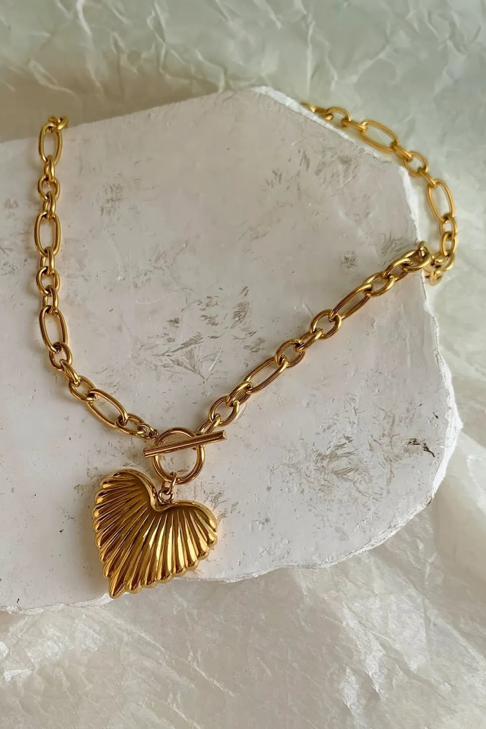 Gold chain bracelet with a heart-shaped charm on a light stone background