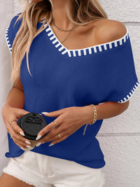 Woman wearing a blue off-shoulder top with white trim, holding a black cup against a light gray background.